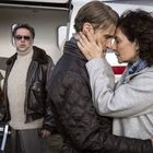 Zwei Menschen umarmen sich innig vor einem Flugzeug. Eine dritte Person steht im Hintergrund neben dem Flugzeug.