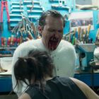 Ein Mann in einem weißen Pullover sitzt mit blutigem Gesicht in einer chaotischen Werkstatt, während eine Frau vor ihm ist.