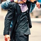 Ein Mann in einem dunklen Anzug wird gestützt, mit einem blutverschmierten Gesicht, und ein buntes Taschentuch ist sichtbar.