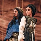 Zwei Frauen in traditioneller Kleidung, eine trägt ein blaues Tuch, die andere hat ein aufwendiges schwarzes Gewand.