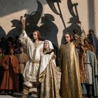 Keine Texte erkennbar. Eine historische Szene, Menschen in mittelalterlicher Kleidung heben die Hand, Schatten von Kriegern.