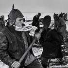 Personen in Winterkleidung arbeiten draußen im Schnee mit Schaufeln. Eine Figur trägt eine Mütze mit spitzem Ende.