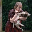 Eine ältere Frau hält einen nassen Hund im Regen. Sie wirkt besorgt und trägt nasse Kleidung.