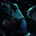 Zwei Personen mit blutverschmierten Gesichtern in einer düsteren Umgebung, Spannung und Besorgnis spiegeln sich wider.