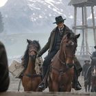 Keine sichtbaren Texte. Szene mit Reitern in einem Berggebiet, Männer mit Hüten und Mänteln, Holzturm im Hintergrund.