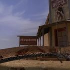 „HOTEL“ und „PAWNBROKER“ sind auf Gebäuden zu lesen. Ein Mann steht auf dem Vordach eines Hotels, vorne eine große Schlange.