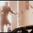 Ein brennender Mann geht durch eine Tür. Es ist dunkel, das Feuer leuchtet hell um ihn herum.