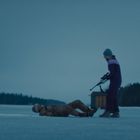 Keine sichtbaren Texte. Zwei Menschen auf einem zugefrorenen See; einer liegt, der andere steht mit einer Waffe.