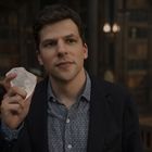 Ein Mann in einem formellen Hemd hält einen groben Kristall. Der Hintergrund hat eine bibliotheksähnliche Atmosphäre.