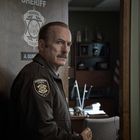 "Sheriff", "Normal County", "A. Gunderson" steht auf einem Türschild. Ein Mann in Sheriff-Uniform mit Donut in der Hand.