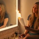Ich kann die Person nicht identifizieren. Eine Frau sitzt vor einem Spiegel, hält ein brennendes Papier in der Hand im Badezimmer.
