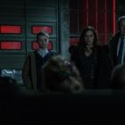 Rotes AVIA-Logo rechts. Drei Personen, zwei Erwachsene, ein Kind, in dunkler Kleidung, mit ernsten Gesichtern in einer dunklen Garage.