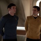 Zwei Personen in einem Raumschiff mit Uniformen; eine in Blau, die andere in Gelb. Beide tragen ein Abzeichen.