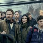 Eine Gruppe von Menschen schaut ernst in eine Richtung. Sie tragen warme Kleidung und befinden sich in einer belebten Umgebung.