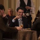 Der Sekt hat die Aufschrift "Cruiser". Eine lebhafte Dinnerparty mit lachenden Personen, einer hält ein Glas Bier.