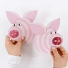 Zwei Hände halten rosa und weiß gestreifte Schweinsköpfe aus Papier mit Knopfnasen und Ohren in Pastelltönen.