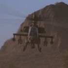 Ein Kampfhubschrauber fliegt in einer Wüstenlandschaft mit Bergen im Hintergrund, bei klarem Himmel.
