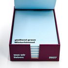 Text: „gleißend graue Winterhimmel“, „was wir lieben: 2027“. Eine geöffnete Box mit hellblauen Notizblättern.