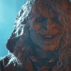 Ein Monster mit zerfurchtem Gesicht und langen Haaren lächelt in einem blauen, leicht nebligen Raum.