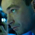 Ein Mann mit intensivem Blick zieht die Aufmerksamkeit auf sich, während eine zweite Person im Hintergrund telefoniert.