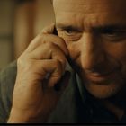 Ein Mann mittleren Alters telefoniert und lächelt leicht. Sein Gesicht ist nah aufgenommen und konzentriert.
