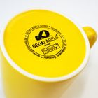 Auf einer gelben Tasse steht: "GEDA LABELS GmbH", "www.gedalabels.de", "Germany" und eine Adresse in Hildesheim.