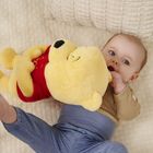 Ein Baby liegt in einem Bett und hält ein gelbes Plüschtier mit rotem Oberteil.