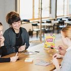 Vier Personen sitzen an einem Tisch und spielen ein Spiel namens "Ditzo!". Sie wirken konzentriert und fröhlich.