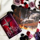 „Dire Bound“, ein Roman von Sable Sorensen. Ein offenes Buch zeigt einen Reiter auf einem weißen Wolf. Umgeben von Blumen.