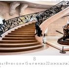 Treppenhaus. Darunter ein geschwungenes Treppenhaus mit verziertem, schwarzem Geländer und einer Skulptur rechts.