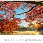 "Sonnenaufgang" steht unten links. Herbstbaum mit roten Blättern ragt über einen nebligen See, im Hintergrund Berge.