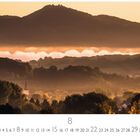 Titel: "Sonnenaufgang am Rhein". Unten Monatsübersicht August. Landschaft mit nebelbedeckten Hügeln und Kirchturm im Abendlicht.