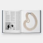 Text: "Faux Pearl Necklace, C. 1950s". Ein aufgeschlagenes Buch zeigt links Text und Foto einer Mutter mit Kind, rechts eine Perlencollier.