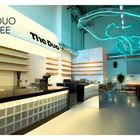 "The Duo Coffee Shop" in Queens, NY. Moderne Einrichtung mit geschwungener Lichtinstallation und eleganten Regalen.