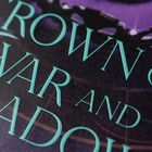 Text: "CROWN OF WAR AND SHADOW". Ein Abschnitt einer Krone ist im Hintergrund zu sehen.