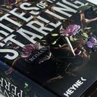 „Rites of the Starling“, „Roman“, „Befreie das M“, „Heyne“. Dunkles Cover mit Lilien und Dolch.