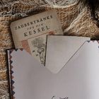 „Zaubertränke für den Kessel“ steht auf einem alten Buch. Es liegt auf einem Tisch, umgeben von Netz und Papier.