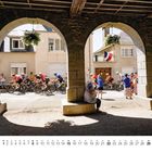 8, Monatstage 1-31. Radfahrer fahren durch einen Torbogen. Zuschauer am Straßenrand, eine französische Fahne weht.