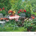 August. Ein blühender Garten mit einem Tisch, Stühlen und üppigen Blumenarrangements.