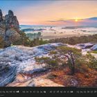 08, Kalender, felsige Landschaft bei Sonnenaufgang, Bäume und Nebel in der Ferne, sonnige Stimmung.