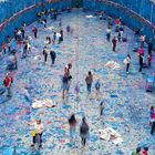 Viele Menschen bemalen eine große blaue Fläche mit bunten Farben. Die Szene wirkt lebendig und kreativ.