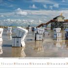 Kalenderblatt für August 2023. Strandkörbe auf nassem Sand, rechts ein Gebäude auf Stelzen; darüber ein Himmel mit Wolken.