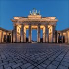 Berliner Sehenswürdigkeit: Das Brandenburger Tor bei Abenddämmerung, Säulen und Quadriga beleuchtet, blauer Himmel.