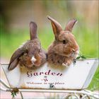 Der Text "Garden - Welcome to our place" ist auf einem Gefäß mit zwei Kaninchen darin. Im Hintergrund ist Gras.