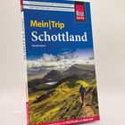 Reiseführer "Mein|Trip Schottland", blaues Cover, Person wandert in grüner Hügellandschaft, Reise Know-How Logo.