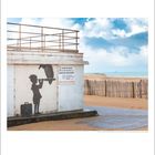 PLAGE DE CALAIS, Schild auf hellem Gebäude. Silhouette eines Mädchens mit Trompete, Koffer daneben. Strand und Meer im Hintergrund.