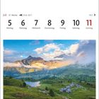 Kalenderdaten für Juli mit Wochentagen. Malerische Landschaft mit Bergen, Wolken und einem kleinen Dorf nahe einem See.