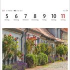 Kalender: Juli, Woche 27, 21.6.–22.7., Tage 5–11. Historische Fischersiedlung, blühende Gärten vor alten Häusern.