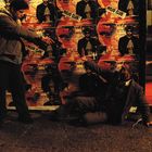 Text: „Mojo Club“ auf mehreren Postern im Hintergrund.  
Szene: Ein Mann zeigt auf einen anderen, der am Boden sitzt.