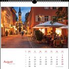 Kalender für August. Eine abendliche Straßenszene mit gemütlichen Cafés und einer Kirche im Hintergrund.